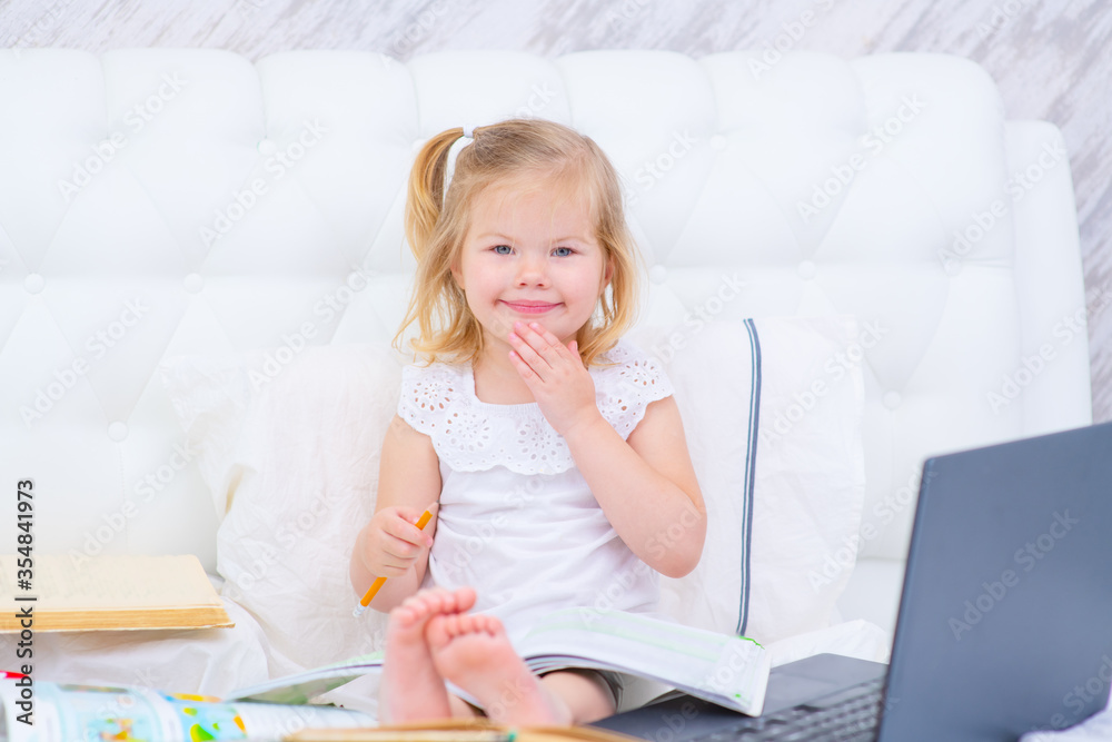 Girl with a smile is engaged while sitting on her bed using a laptop Girl with a smile is engaged while sitting on her bed using a laptop