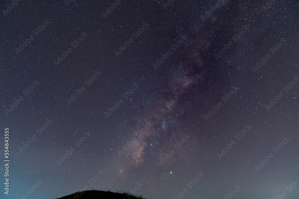 Fototapeta premium Silhouette of a man with a flashlight, observing beautiful, wide blue night sky with stars and Milky way galaxy. Astronomy, orientation, clear sky concept and background.