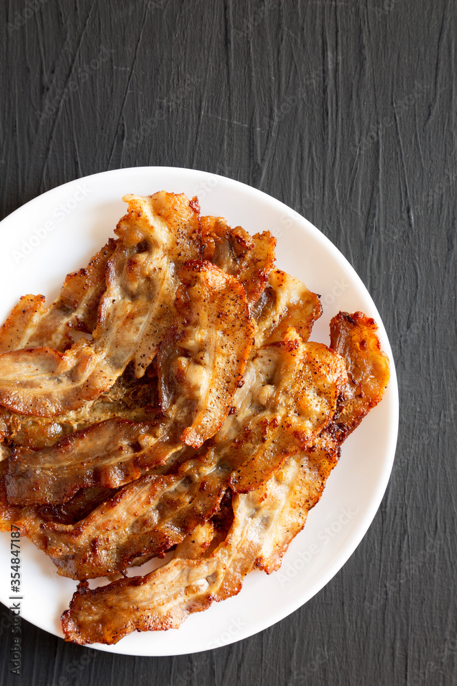 Homemade Fried Bacon on a white plate on a black background, top view. Overhead, from above, flat lay. Homemade Fried Bacon on a white plate on a black background, top view. Overhead, from above, flat lay.