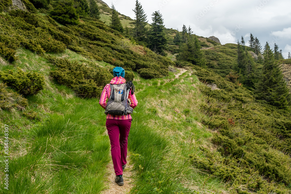 Young girl with backpack on her back on a mountain path hiking alone in nature. Thickly dressed woman climbing a winding path in the Ciucas Mountains in Romania.