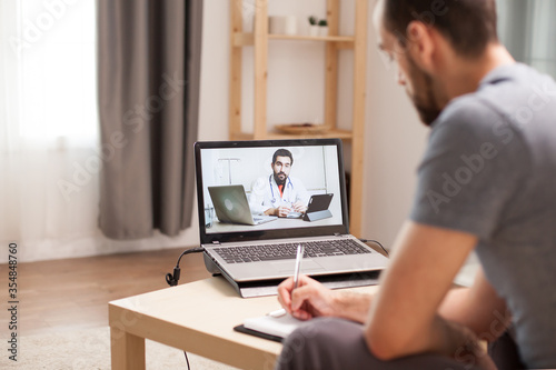 Male taking notes on clipboard in a video call with his doctor during consultation in time of quarantine.