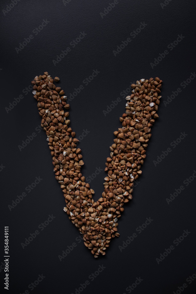 Letter 'V' written with buckwheat On gray background, top view, copy space. Food supplies crisis, food donation on quarantine isolation period Letter 'V' written with buckwheat On gray background, top view, copy space. Food supplies crisis, food donation on quarantine isolation period