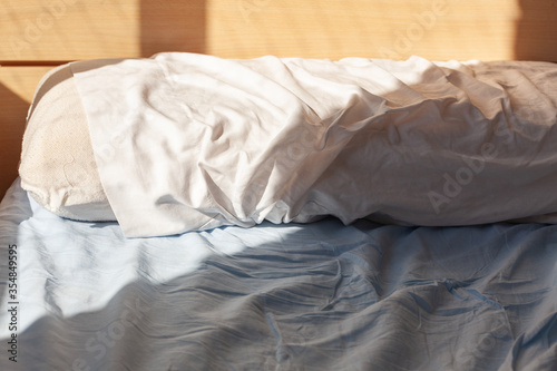 Wake up concept: pillow on unmade bed with wrinkles on sheets lit by morning light