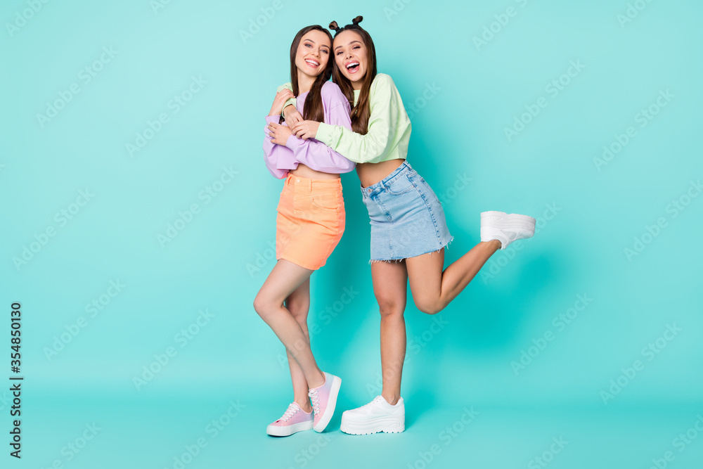 Full length photo of two cheerful ladies friends cool look clothes hugging students wear cropped sweaters naked belly short skirts shoes isolated pastel teal color background Full length photo of two cheerful ladies friends cool look clothes hugging students wear cropped sweaters naked belly short skirts shoes isolated pastel teal color background