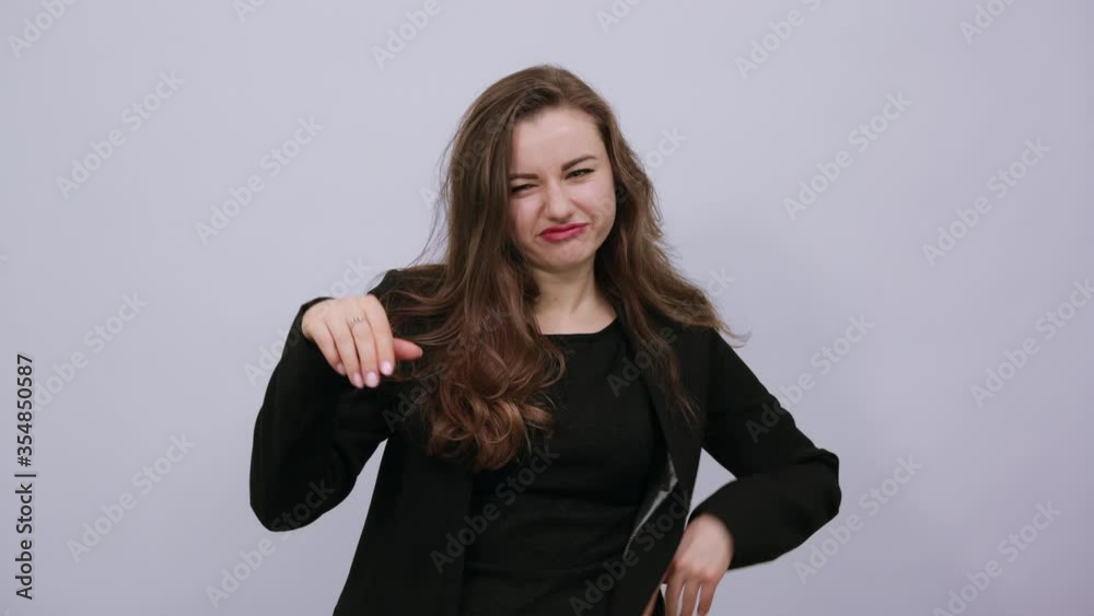 Young Attractive Woman Brunette In In A Black T-Shirt, Sweater On White Background, Dissatisfied Female Returned Thumb Finger To Bottom And Demonstrates Disagreement. Opposition, People's Protest Young Attractive Woman Brunette In In A Black T-Shirt, Sweater On White Background, Dissatisfied Female Returned Thumb Finger To Bottom And Demonstrates Disagreement. Opposition, People's Protest