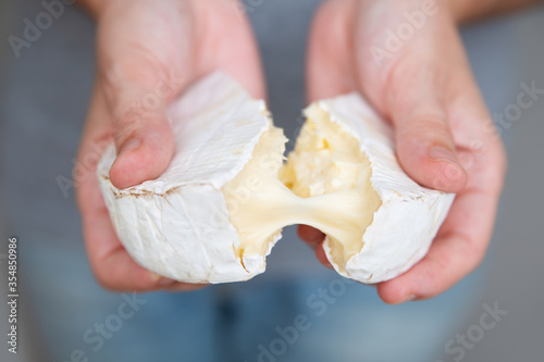 Female hands tearing soft cheese into two parts. Tasty brie or camembert. Studio shot. Selective focus. Front view. Dairy meal and cooking on isolation concept for flyers and banners