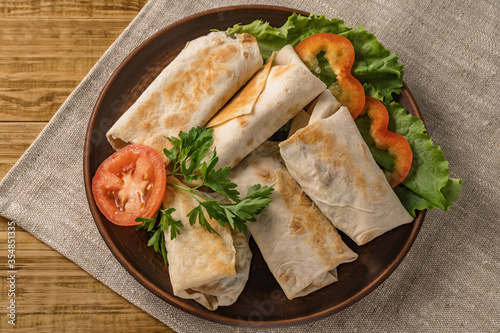 Hot pita bread wrapped with cheese and vegetables and greens on a rustic plate.