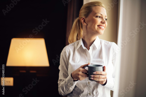  Businesswoman relaxing in hotel room. Young beautiful woman drinking coffee.