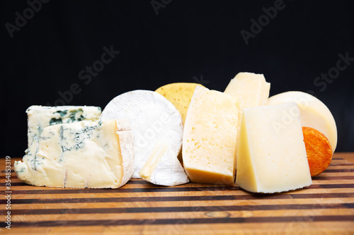 Delicious different cheeses laying on wooden board and isolated on black background. Studio shot. Side view. Dairy meal and cooking on isolation concept for flyers and banners