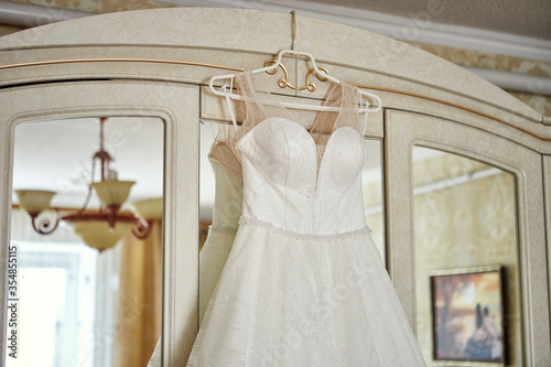 beautiful wedding dress hanging in the room, woman getting ready before ceremony