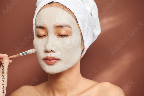 Attractive young woman applying cosmetic mask on her face.