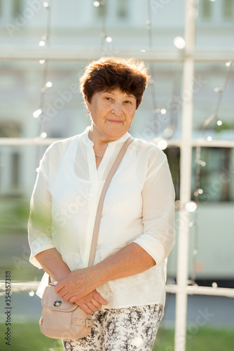 Portrait of modern stylish mature sixty year old grandmother with neat hairstyle, posing outdoor looking at camera with joyful happy smile.