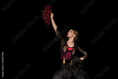 beautiful dancer looking at fan while dancing flamenco isolated on black