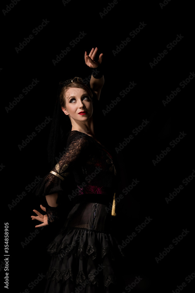 elegant flamenco dancer looking away and dancing isolated on black