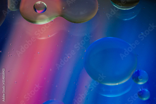 Bubbles of vegetable oil in clear water on a glass and transparent lid from a frying pan on colored paper.