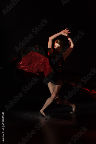 pretty young dancer with hands above head dancing flamenco on black