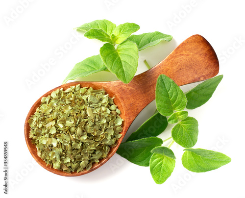 dried oregano flakes in the wooden spoon, with fresh oregano twigs, isolated on white background, top view