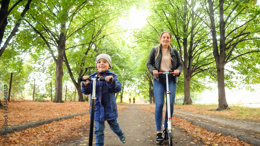 Portrait of smiling little boy enjoys riding on scooters with his mother at park Portrait of smiling little boy enjoys riding on scooters with his mother at park