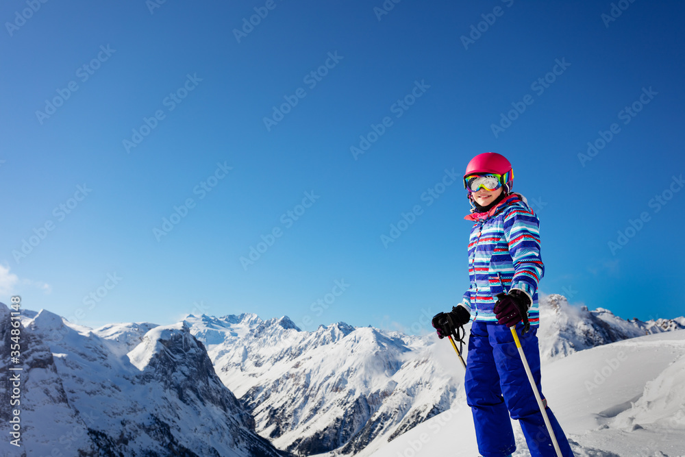 Close portrait of a ski girl stand in colorful vivid sport clothes, helmet and glasses over Alps mountain tops view
