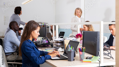 Focused female working with laptop in busy modern office
