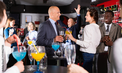 Cheerful male and female colleagues having fun on corporate party in bar