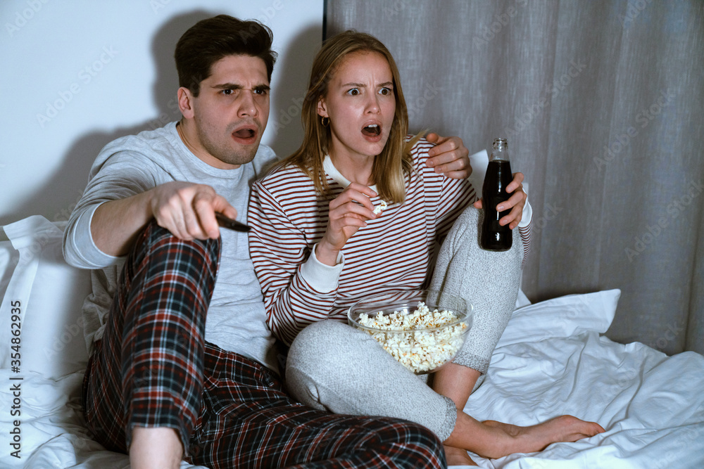 Portrait of shocked caucasian couple watching tv and eating popcorn Portrait of shocked caucasian couple watching tv and eating popcorn