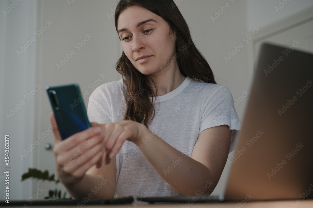 young freelancer woman using her smartphone while working from home young freelancer woman using her smartphone while working from home