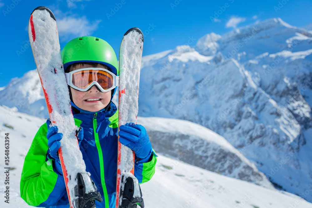 Happy boy hugging a pair of ski standing over mountains smiling, close up portrait
