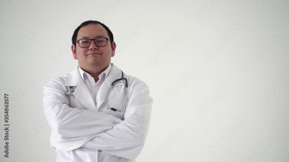 Asian doctor in a white medical coat and glasses, with a stethoscope, crosses his arms in front of him and smiles shaking his head, on a white background Asian doctor in a white medical coat and glasses, with a stethoscope, crosses his arms in front of him and smiles shaking his head, on a white background