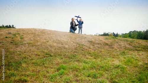Happy young mother with little son standing on hill top and throwing toy airplane