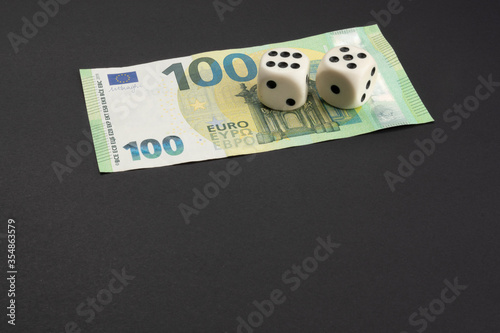 Money, finance and gambling concept: European 100 (hundred) EUR, Euro banknote at top of frame on black background with copy space. Two white dice on top showing the numbers 5 and 6 photo