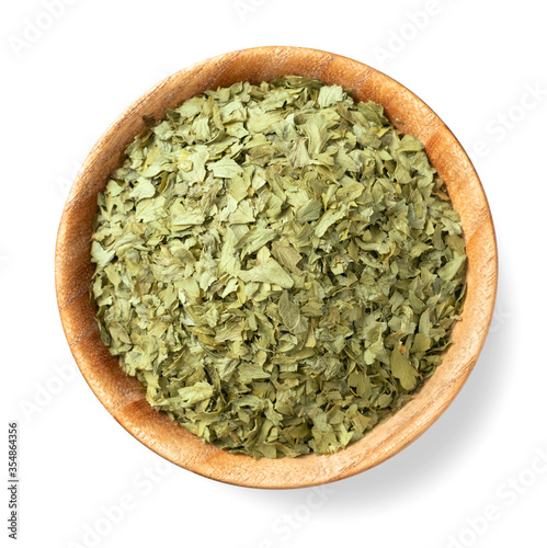 dried parsley flakes in the wooden bowl, isolated on white background, rop view
