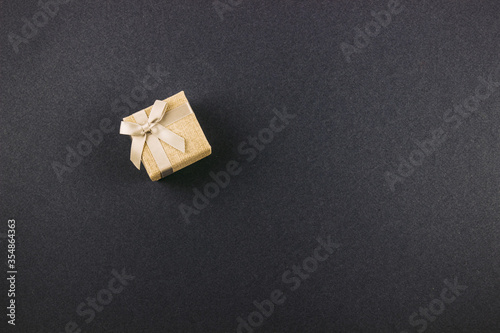 Small gift box square sand color tied with a bow on a gray background. The concept of gifts