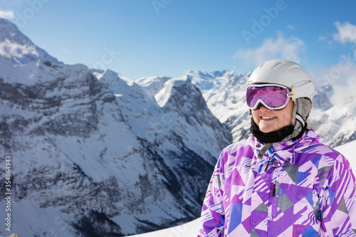 Close portrait of happy teen girl smile wear cute winter ski outfit glasses, helmet over mountain peaks © Sergey Novikov