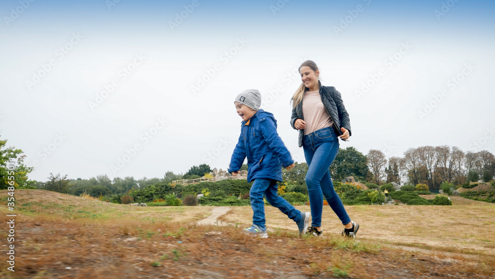 Happy smiling little boy with young mother racing up on the hill in autumn park Happy smiling little boy with young mother racing up on the hill in autumn park