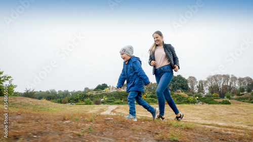 Happy smiling little boy with young mother racing up on the hill in autumn park