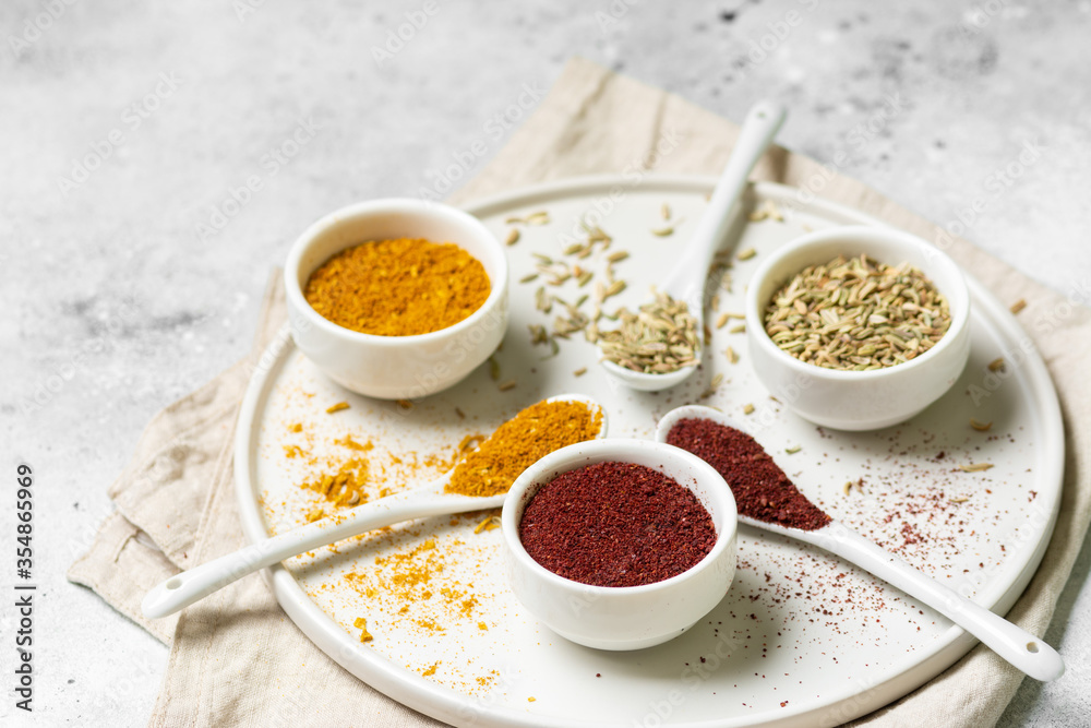 Spices and condiments in white bowls on a light gray table. Turmeric, ginger, curry, fennel and sumac in white bowls. Spices close up Spices and condiments in white bowls on a light gray table. Turmeric, ginger, curry, fennel and sumac in white bowls. Spices close up
