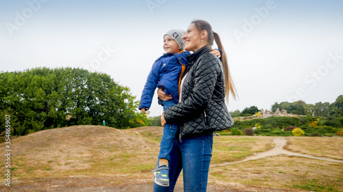 Portrait of happy smiling young mohter holding and embracing her little son on field at park