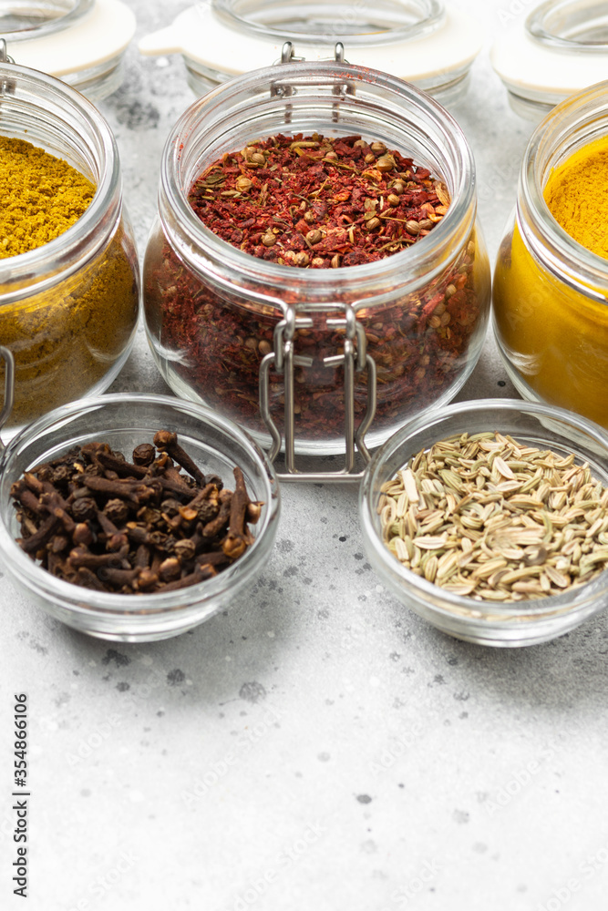 Spices and condiments in glass jars on a light gray table. Spices close-up with space for text