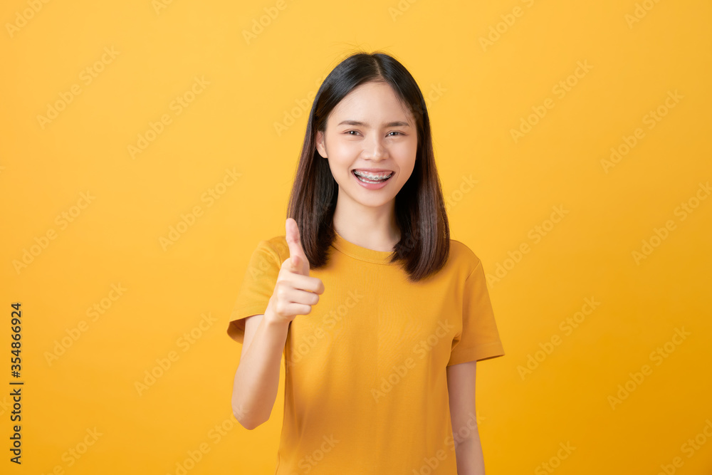 Young smiling Asian woman stand and pointing finger to copy space on yellow background. Young smiling Asian woman stand and pointing finger to copy space on yellow background.