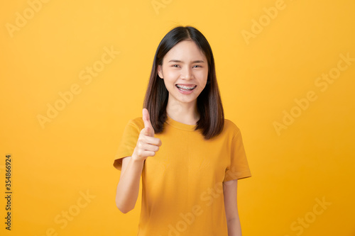 Young smiling Asian woman stand and pointing finger to copy space on yellow background.