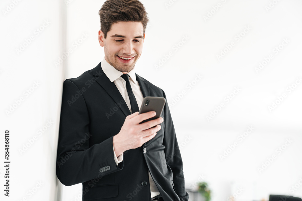 Image of smiling businessman wearing black suit using mobile phone Image of smiling businessman wearing black suit using mobile phone