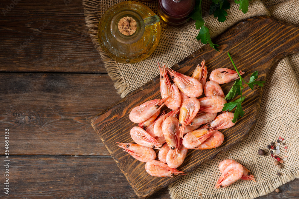 Shrimp on a wooden Board on a brown wooden table. Lots of prawns on the serving Board. Shrimp close-up. Top view with space for text