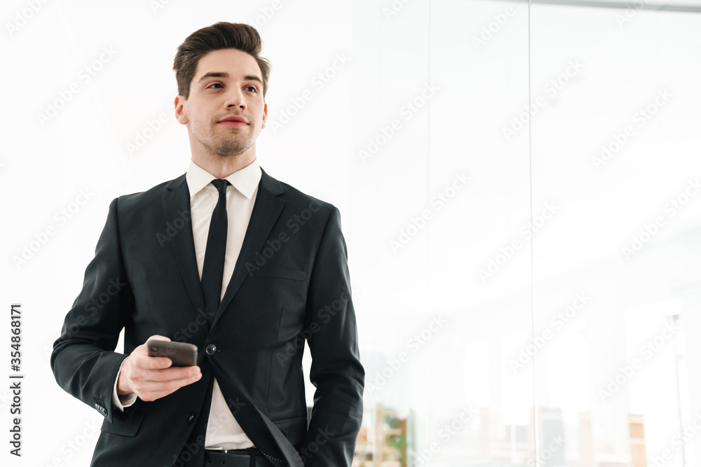 Image of serious businessman wearing black suit using mobile phone Image of serious businessman wearing black suit using mobile phone