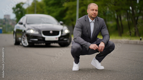 Elegant man in a suit without tie next to a car on the highway