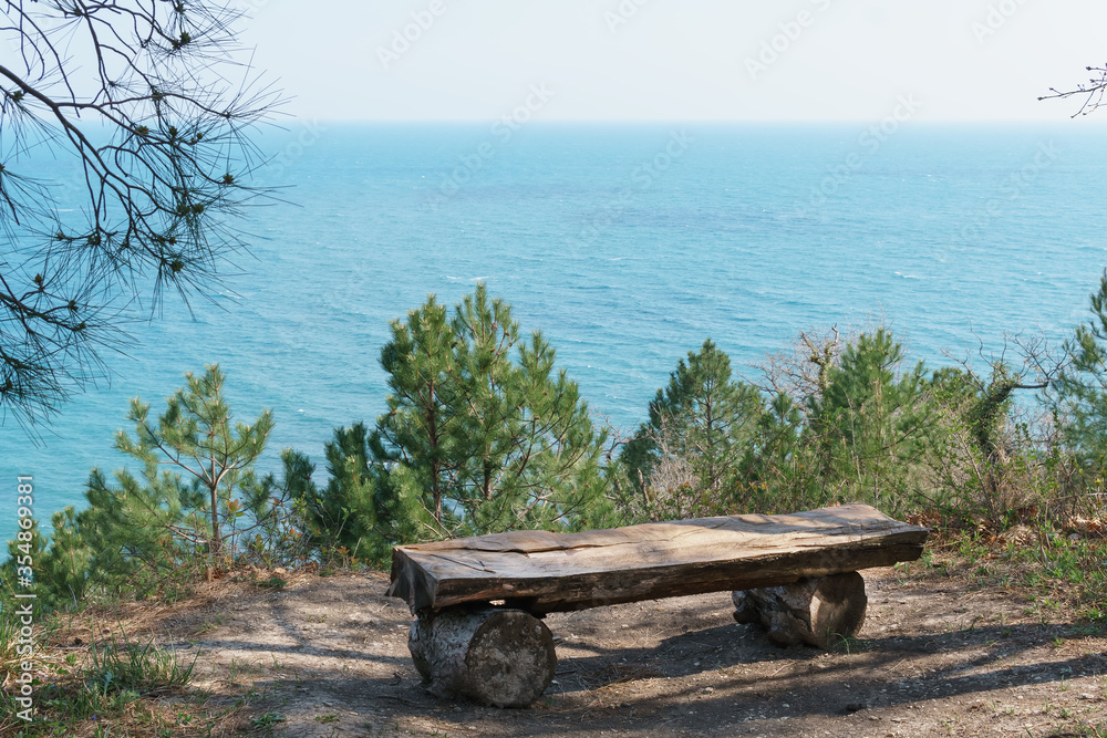 A single bench made of natural wood in the forest with a view of the sea.