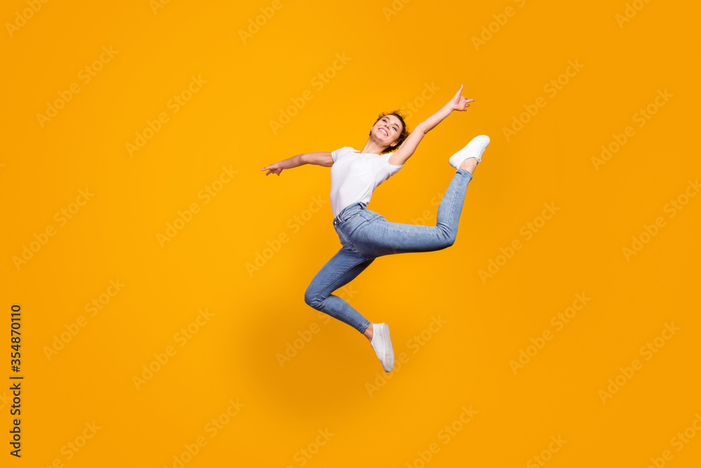 Full length profile photo of amazing lady flexible body raising leg artist dancer performance jumping high up wear white t-shirt jeans isolated yellow bright color background
