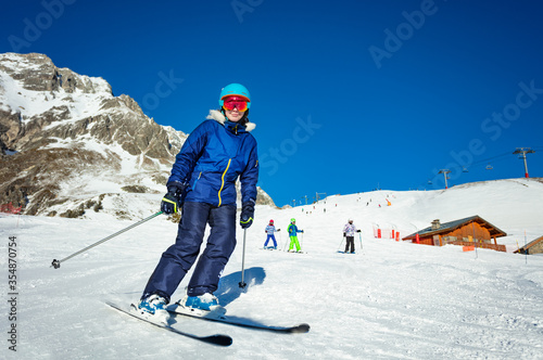 Portrait of teen girl in colorful outfit ski with kids on background on Alpine resort on sunny winter day