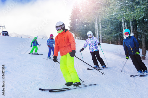 Group of children ski on the hill with friends on Alpine resort over forest on background