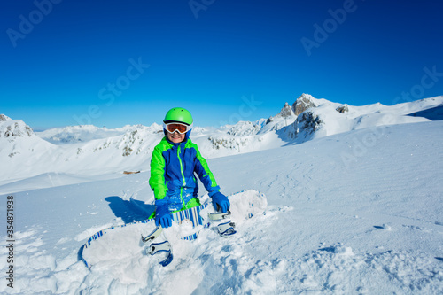 Wide mountain panorama and cute little smiling boy hold snowboard in hand aside, view from above with mask off